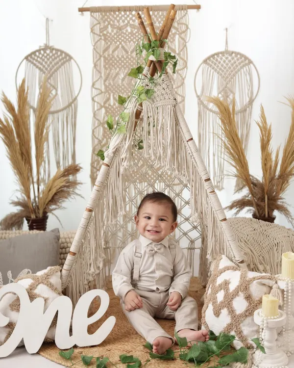 A handsome little man celebrating his first birthday with a full boho setup. The macrame teepee and natural tones create a stylish backdrop for this milestone portrait.