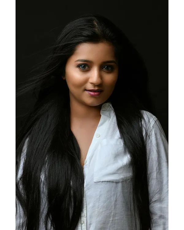 A simple and beautiful headshot with a clean, dark background. The wind in her hair adds a dynamic element, while her direct gaze creates a strong connection with the viewer.