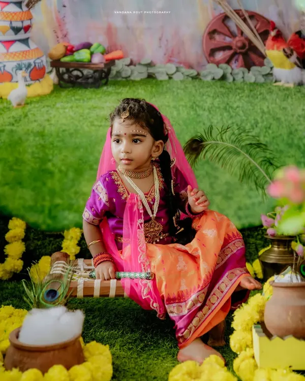 A beautiful portrait of a little girl dressed as Radha for a Janmashtami celebration. The vibrant set, complete with marigolds and a pot of butter, brings the festival to life.