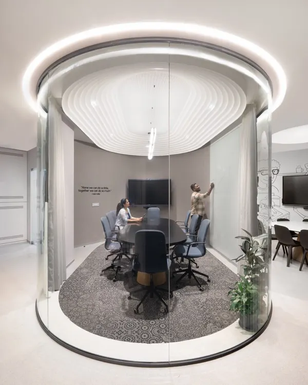 This unique cylindrical glass meeting pod is a centerpiece of the office. It offers acoustic privacy for meetings while its transparency maintains the open-plan feel. The sculpted ceiling and halo light add a futuristic touch.