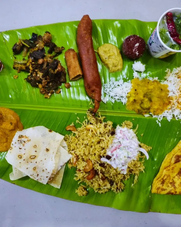A complete traditional South Indian vegetarian meal served on a fresh banana leaf, featuring a colorful assortment of curries, rice, poori, vada, and sweets. This is the heart of our authentic Andhra and Karnataka catering service.