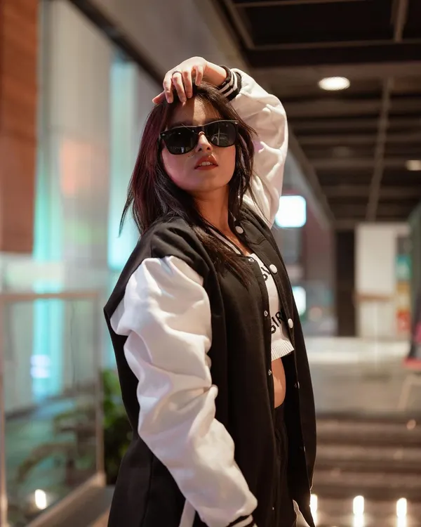 A classic streetwear look featuring a varsity jacket and sunglasses. The shallow depth of field and the model's confident pose create a cool, urban vibe perfect for a youth-focused fashion brand.