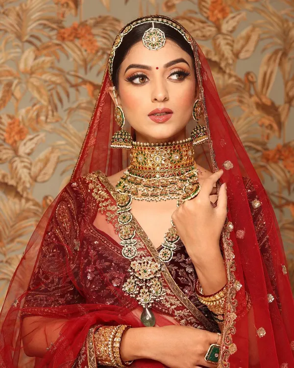 A regal and timeless bridal portrait. This look features a deep red velvet lehenga, complemented by makeup that emphasizes sharp, defined eyes and a perfectly sculpted face, fit for a modern queen.