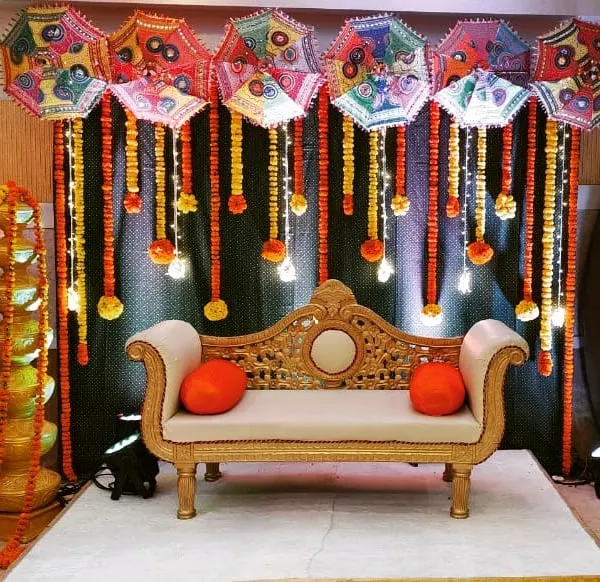 Our popular Haldi setup featuring a backdrop of colourful Rajasthani umbrellas, marigold garlands, and a traditional sofa for the couple. This decor is perfect for festive photos.