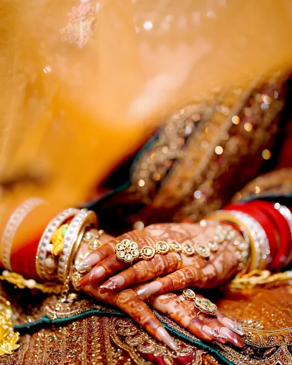 A close-up on the bride's hands, showcasing the intricate henna design, the traditional 'chooda' bangles, and the beautiful hand jewelry.