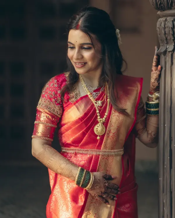 The beautiful bride Madhavi in her red silk saree. Her look features soft, defined eyes and a radiant base, perfect for her wedding ceremony.