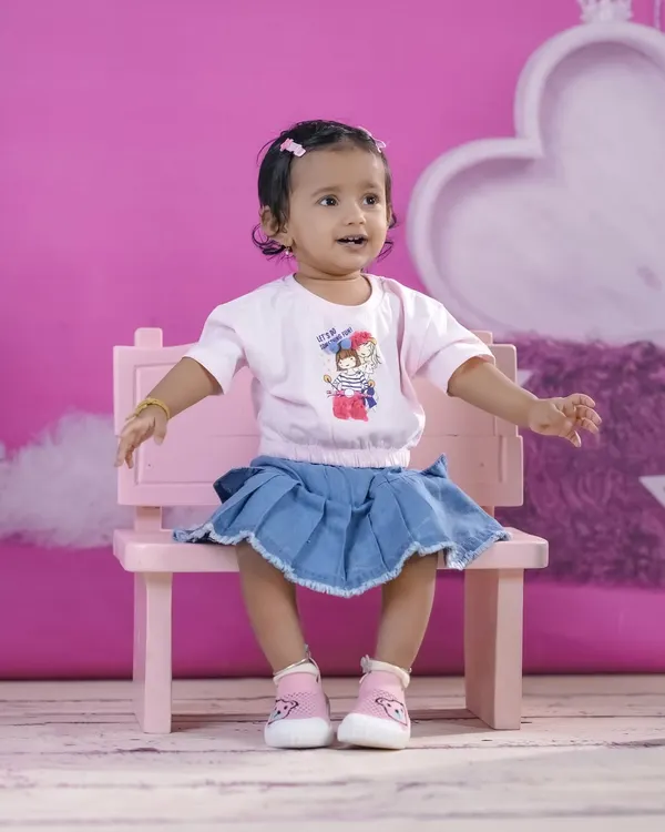 A happy little girl on a pink bench against a matching pink backdrop. Our studio is equipped with a variety of colorful backgrounds.