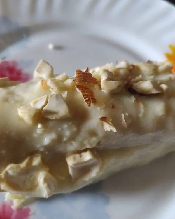 A close-up of a delicious Bread Malai Roll, a creamy Indian dessert soaked in sweetened milk and garnished with chopped nuts.