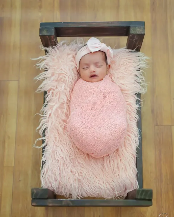 An overhead shot of a newborn sleeping peacefully in a rustic prop bed. The soft pink fur and matching swaddle create a cozy and coordinated look for this studio baby shoot.