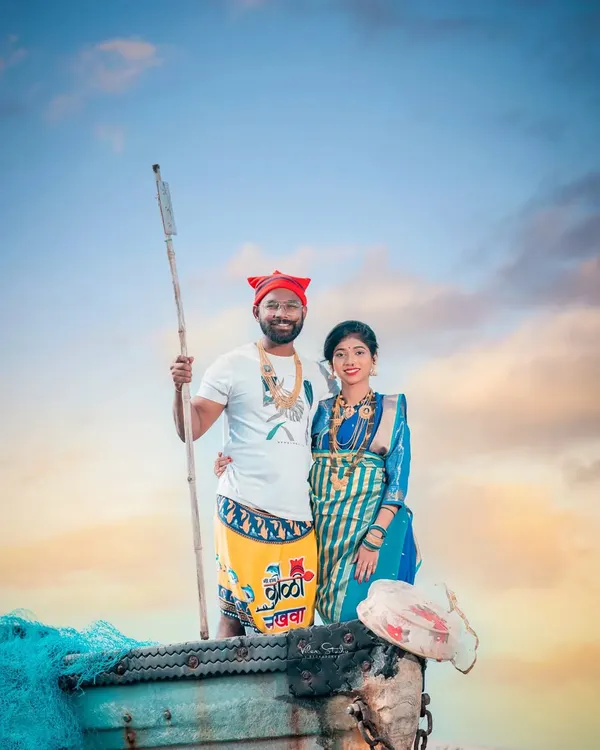This is a classic Agri-Koli themed portrait. The couple stands in a boat, with the groom holding a traditional paddle, dressed in a lungi and Koli cap. It’s a powerful image that celebrates their cultural roots.