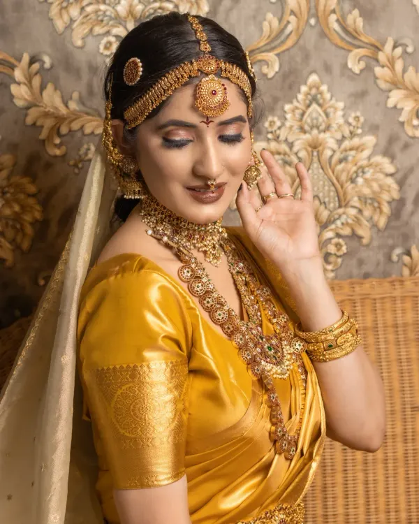 A student's portfolio work featuring a classic South Indian bridal look with a golden silk saree and temple jewellery. The focus here is on creating a radiant, long-lasting base.