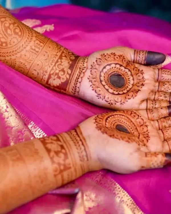 A beautiful bridal mehendi for Anushiya, set against her vibrant pink saree. The design features bold mandalas on the palm and detailed cuff work on the arms, showing how the henna complements the entire bridal look.