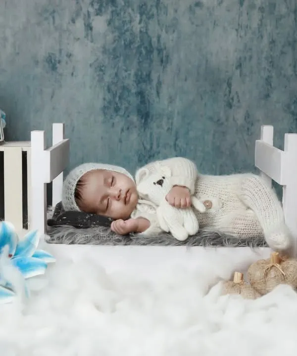 A newborn sleeps peacefully in a miniature bed, dressed in a cozy knit outfit. Our two-month milestone sessions capture how much they've grown in just a few weeks.