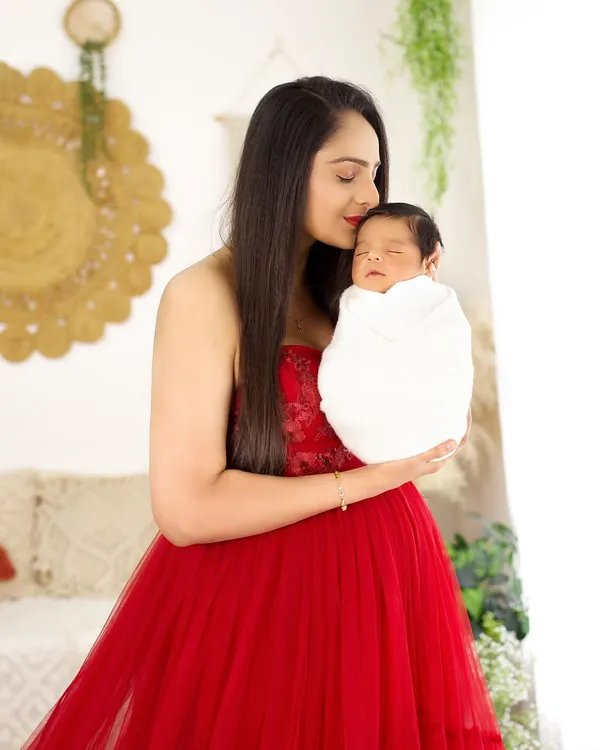 A mother's love captured in a single frame. This portrait of a new mom in a striking red dress holding her sleeping newborn is full of warmth and tenderness.