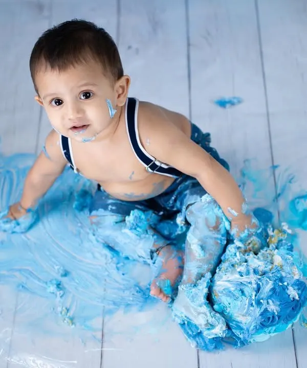 The best part of a cake smash is the pure, messy joy. This little boss baby is having the time of his life with his blue-themed birthday cake.