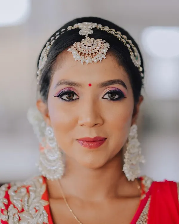 A striking beauty portrait. The focus is entirely on the bride's face, highlighting the bold, colorful eye makeup and the delicate shimmer of her traditional headpiece.