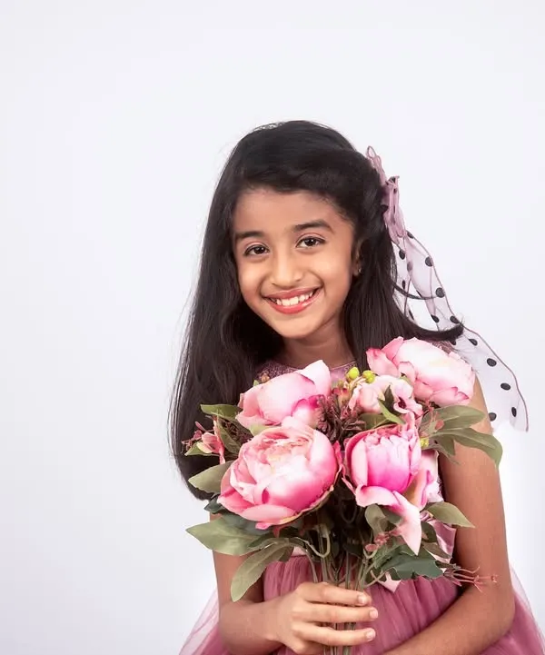 A beautiful studio portrait of a smiling girl holding a bouquet of pink flowers. The simple white background makes her joyful expression the star of the show.