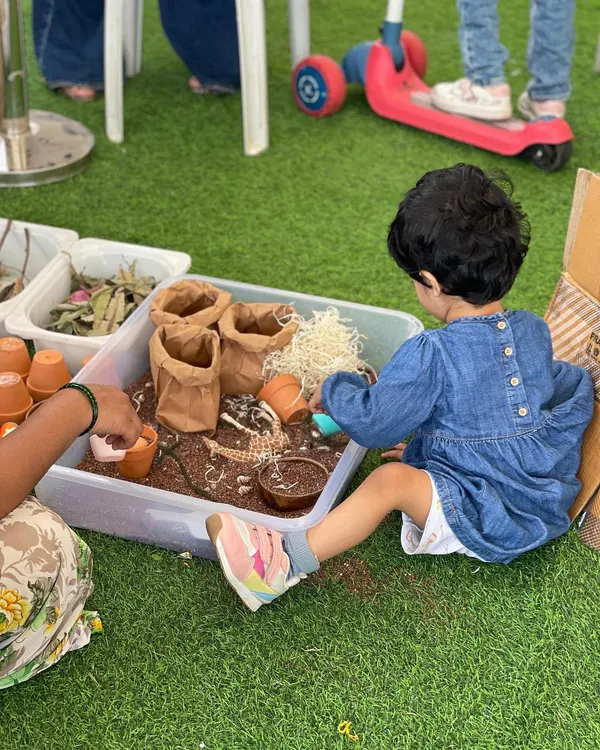 Our sensory play zones are a paradise for toddlers. This little one is exploring a gardening-themed sensory bin, a hands-on activity that is fantastic for developing fine motor skills and engaging their sense of touch.