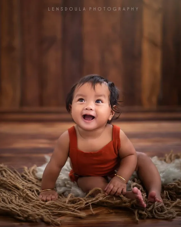 The magic isn't in the props, it's in this smile. A simple wooden backdrop and a soft rug are all that's needed to let this baby's joyful spirit shine through.