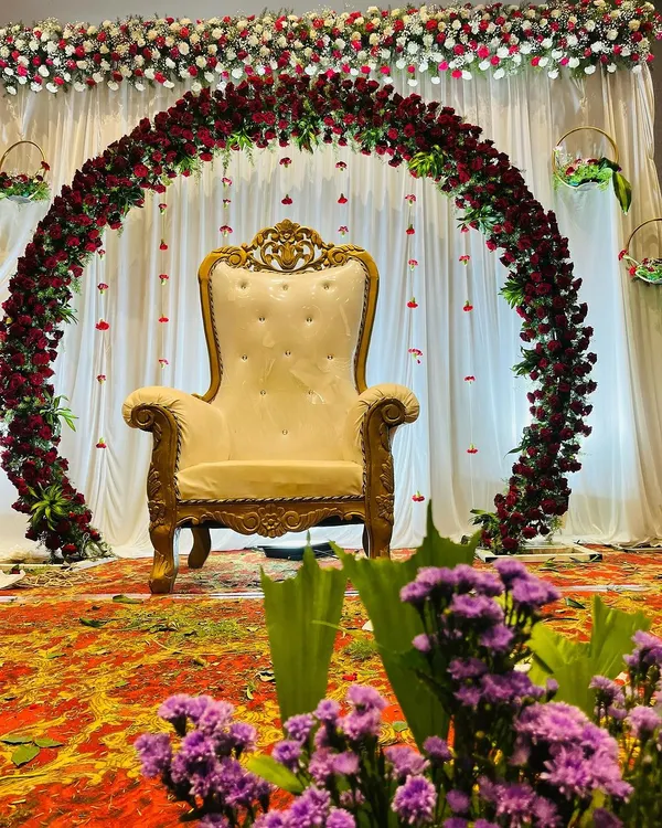 A simple yet elegant floral arch of red roses creates a classic backdrop for a baby shower. The focus remains on the ornate central chair, making the mother-to-be the star of the ceremony.