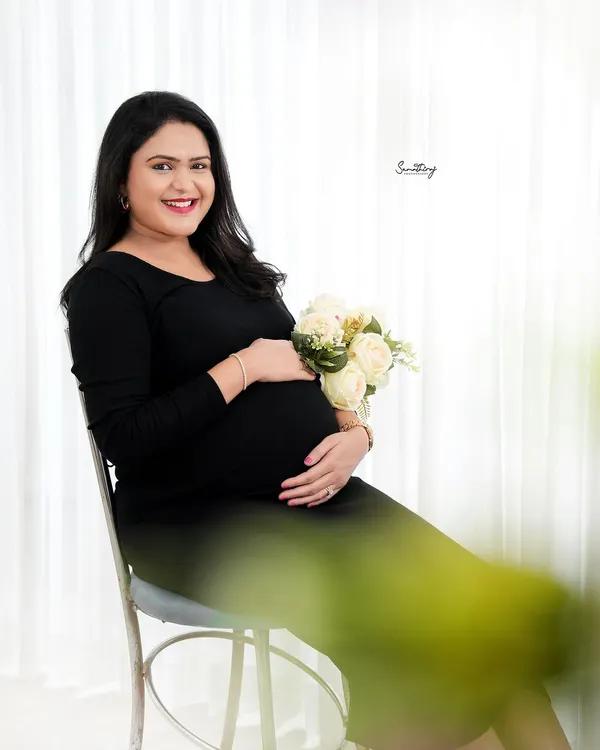 A classic and bright indoor portrait. The simple black dress, paired with a bouquet of white roses, creates a look of timeless elegance and joy.