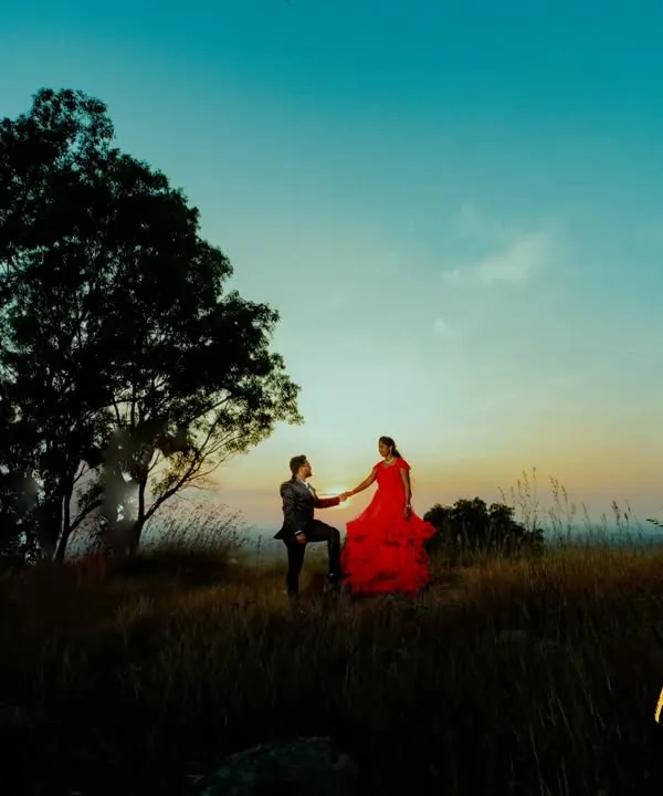 A breathtaking pre-wedding portrait on a hilltop at sunset. The flowing red gown against the twilight sky creates a truly cinematic feel for your love story.