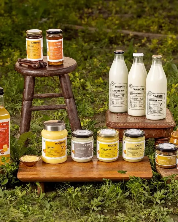 A complete product family shot for Barosi, featuring their range of ghee, oils, and milk in a rustic outdoor setting. This image communicates the brand's farm-fresh and natural ethos by placing the products right in the midst of greenery.