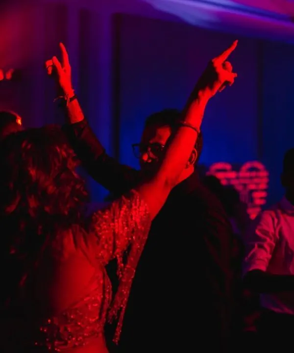 The energy of the sangeet dance floor captured with dramatic red and blue lighting. We use motion blur and creative lighting to convey the vibrant atmosphere of the party.