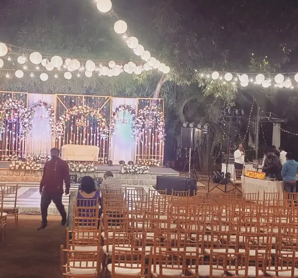 A wide view of an outdoor reception setup at night, featuring a beautifully lit stage and elegant guest seating under string lights.