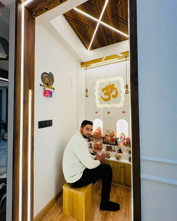 Sitting in a completed mandir at Prateek Laurel. This serene space features a backlit 'Om' symbol, a beautiful wooden ceiling design with profile lights, and ample space for prayer.