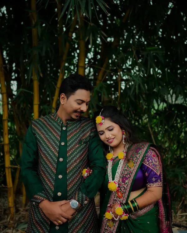 A sweet, candid moment during a Haldi photoshoot. The bride rests her head on the groom's shoulder, both adorned in floral jewelry, sharing a quiet moment before the festivities.