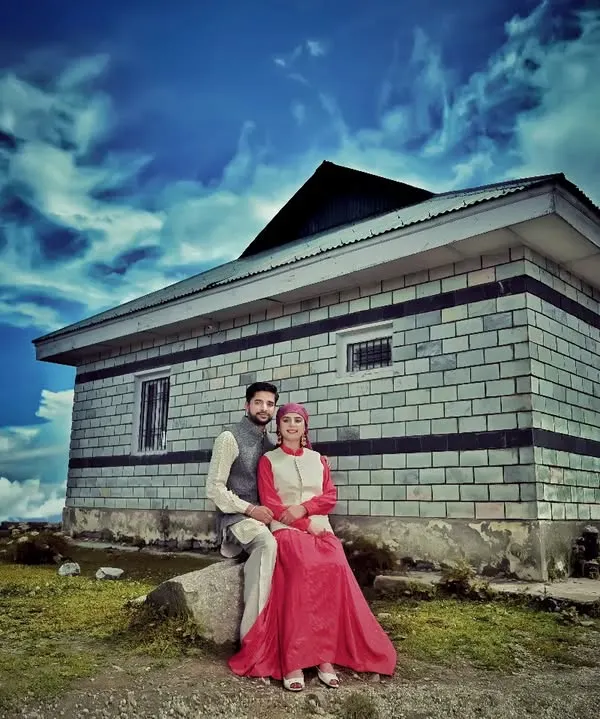 A dramatic pre-wedding portrait featuring a couple in front of a traditional stone house under a striking blue sky. This style of editing and composition creates a powerful, memorable image for your album.