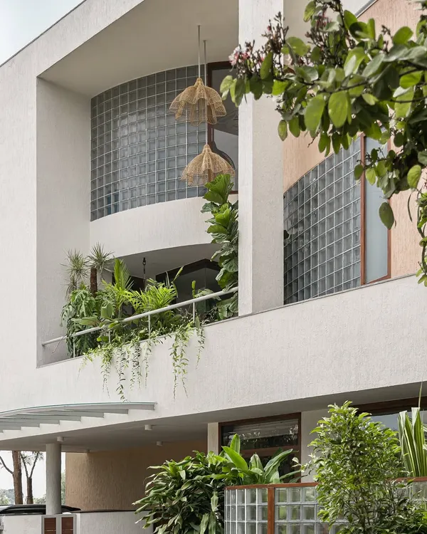 The facade of this villa in Bengaluru showcases our tropical modern style. Deep balconies filled with greenery and large glass block walls create a layered exterior that connects the home with its natural surroundings.
