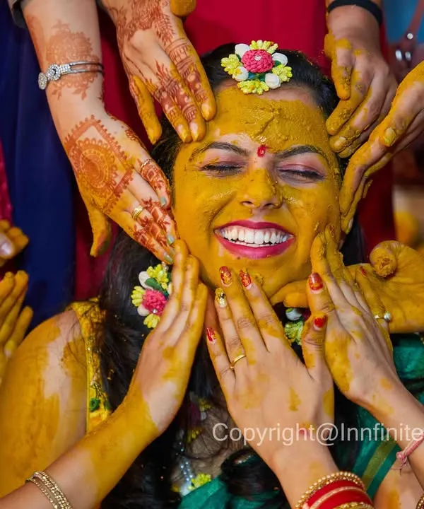 The Haldi ceremony is all about fun and family. This shot, with hands coming from all directions, perfectly captures the joyful chaos and the bride's radiant smile.