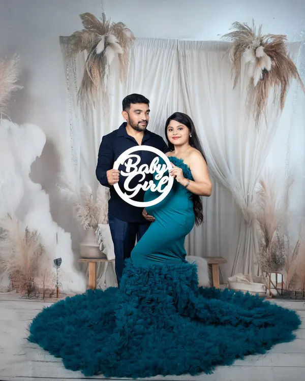 A couple's maternity portrait with the mother-to-be in a stunning teal gown, holding a 'Baby Girl' sign against a dreamy boho backdrop.