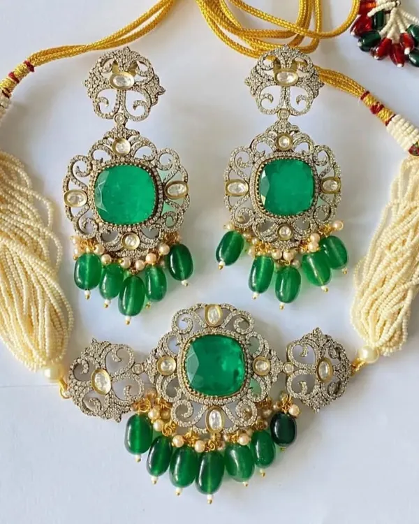 A truly exclusive Victorian-style bridal set in a silver and gold finish with high-quality emerald green stones. This set, including the choker and matching long earrings, is perfect for a grand reception look.