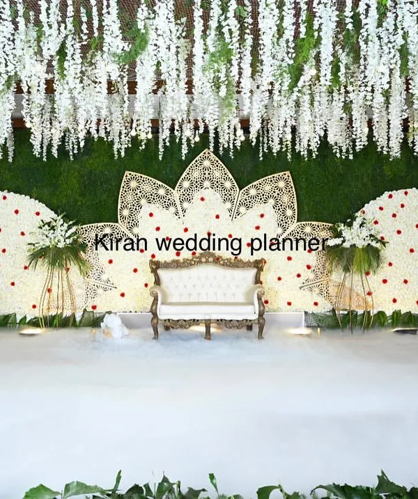 An elegant white floral reception stage featuring two large semi-circular backdrops and a central lotus motif. The addition of low-lying fog creates a dreamy, cloud-like effect for the couple.