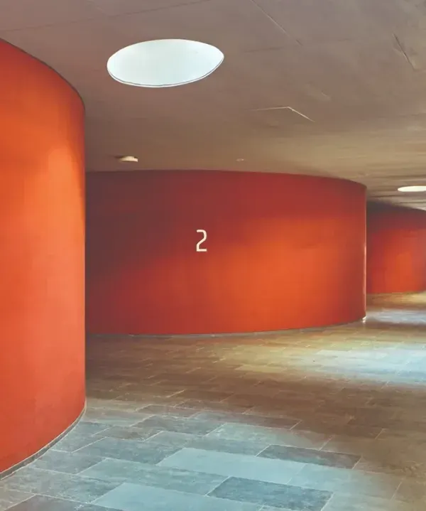 Circular skylights punctuate the ceiling of a corridor, casting pools of natural light onto the floor. This simple gesture transforms a simple circulation space into a dynamic experience, marked by a rhythm of light and dark.