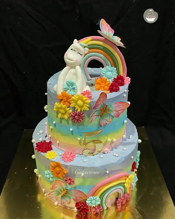 A magical two-tier unicorn cake for a 5th birthday. This 4kg Dutch Truffle cake is decorated with rainbows, colorful flowers, and a sleepy unicorn, all made with buttercream.