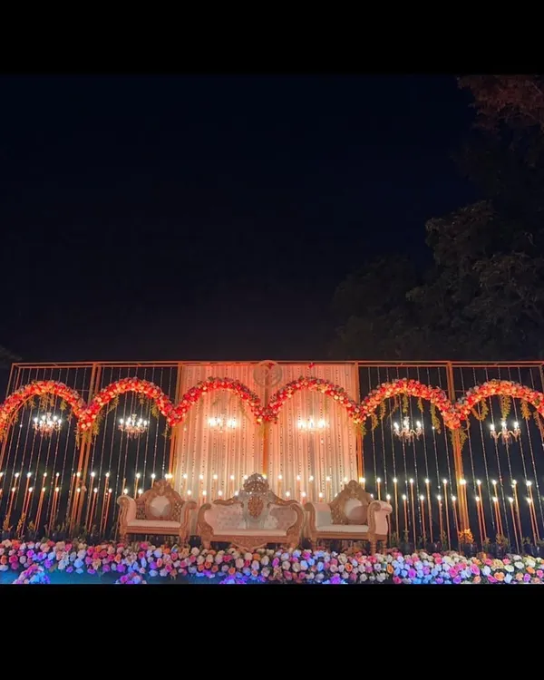 This wide view showcases a complete reception stage setup for a destination wedding in Lonavala. The design features a series of golden arches, elegant chandeliers, and a lush floral base, creating a grand and romantic backdrop for the couple.