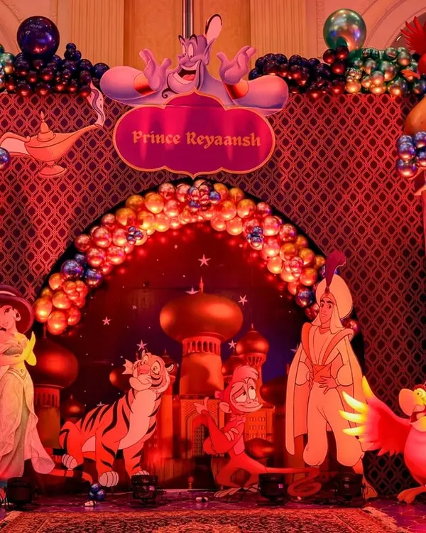 The main photo-op stage for this Aladdin-themed party, featuring a grand arch, a sparkling balloon arrangement, and cutouts of all the main characters.