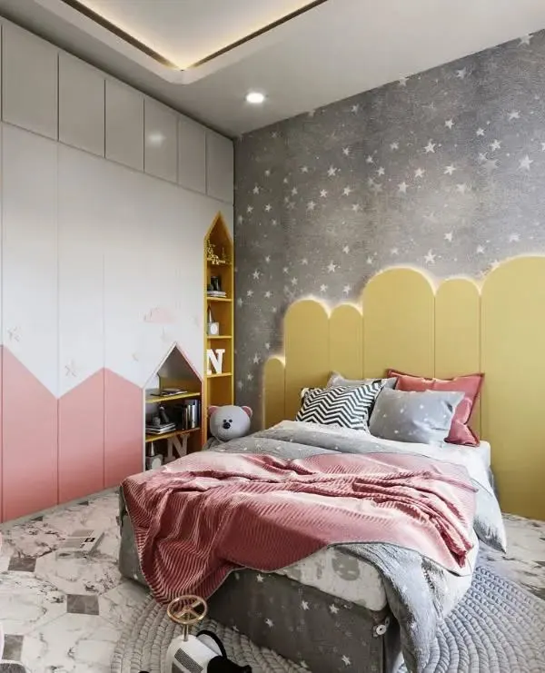 A dreamy bedroom design featuring a cloud-shaped headboard with accent lighting. The room combines soft pink and bright yellow with a starry wallpaper and mountain-themed wardrobe to create a whimsical landscape.