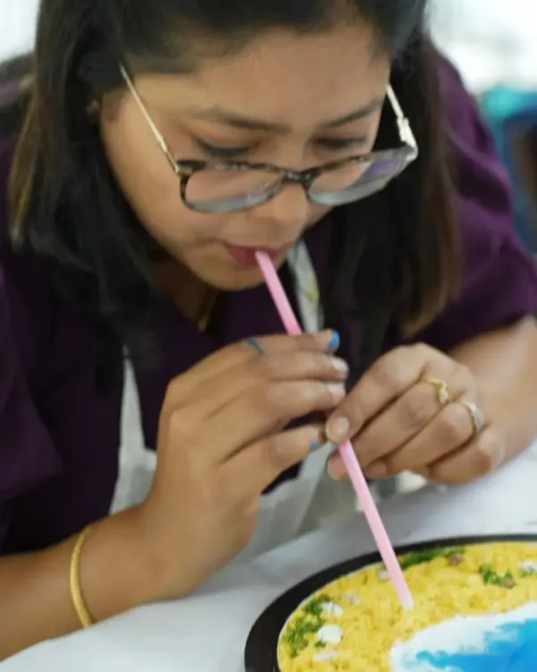 A close-up shot of a participant using a straw to create delicate wave effects in her resin beach art. This simple technique helps make realistic, lacy sea foam on the shore.