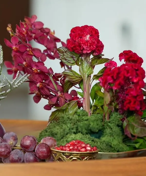 A centerpiece from our 'दाड़म ka Bageecha' theme, featuring a rich palette of red flowers, fresh grapes, and pomegranate seeds in an antique brass bowl. This is where food, art, and nature meet.