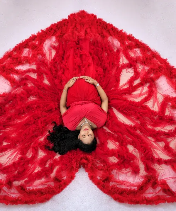 We love creating artistic and memorable shots. Here, we arranged this stunning red ruffled gown into a heart shape for a dramatic overhead portrait, symbolizing the love surrounding the mother-to-be. This is one of our signature studio concepts.