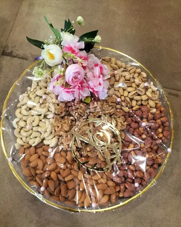 A classic dry fruit platter featuring an assortment of almonds, cashews, walnuts, and pistachios. The arrangement is finished with a custom acrylic monogram and a small floral bouquet, making it an elegant and healthy gift option.
