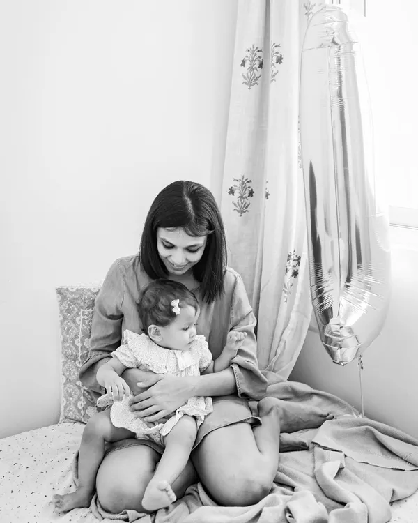 A quiet moment between a mother and her baby, captured in classic black and white. The number '1' balloon in the background marks her special milestone.