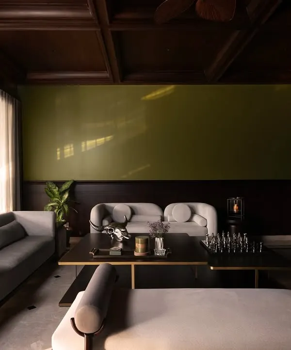 A wide view of the formal living area, where I balanced the dark, coffered teak ceiling with light grey sofas and an olive accent wall. The design creates a sophisticated space for conversation, grounded in traditional architectural elements.