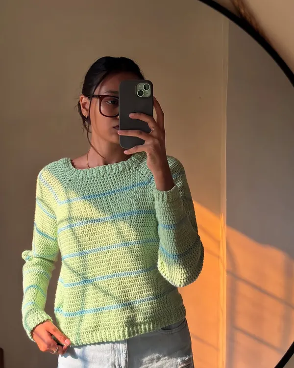 A mirror selfie in the pastel striped sweater. It has a classic crew neck and a relaxed fit that's super comfortable.