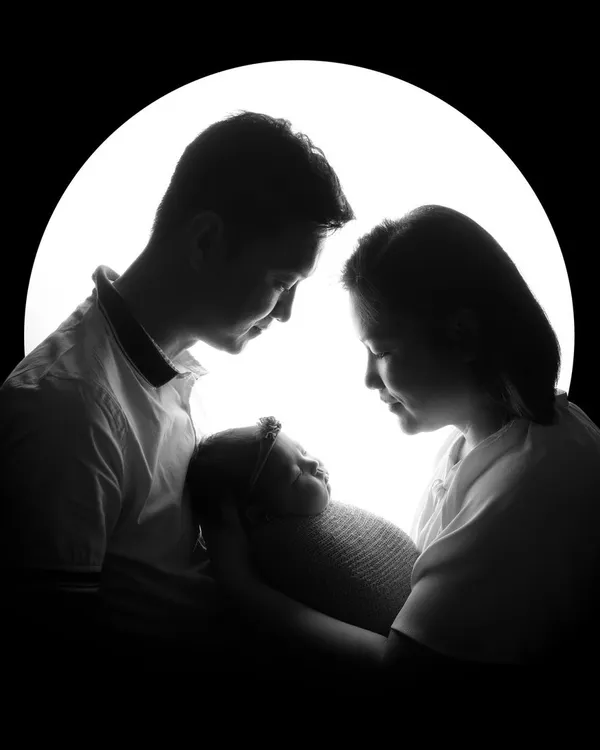 An artistic silhouette of parents admiring their newborn, creating a dramatic and timeless family portrait. This style focuses on the outlines and the emotional connection within the family.